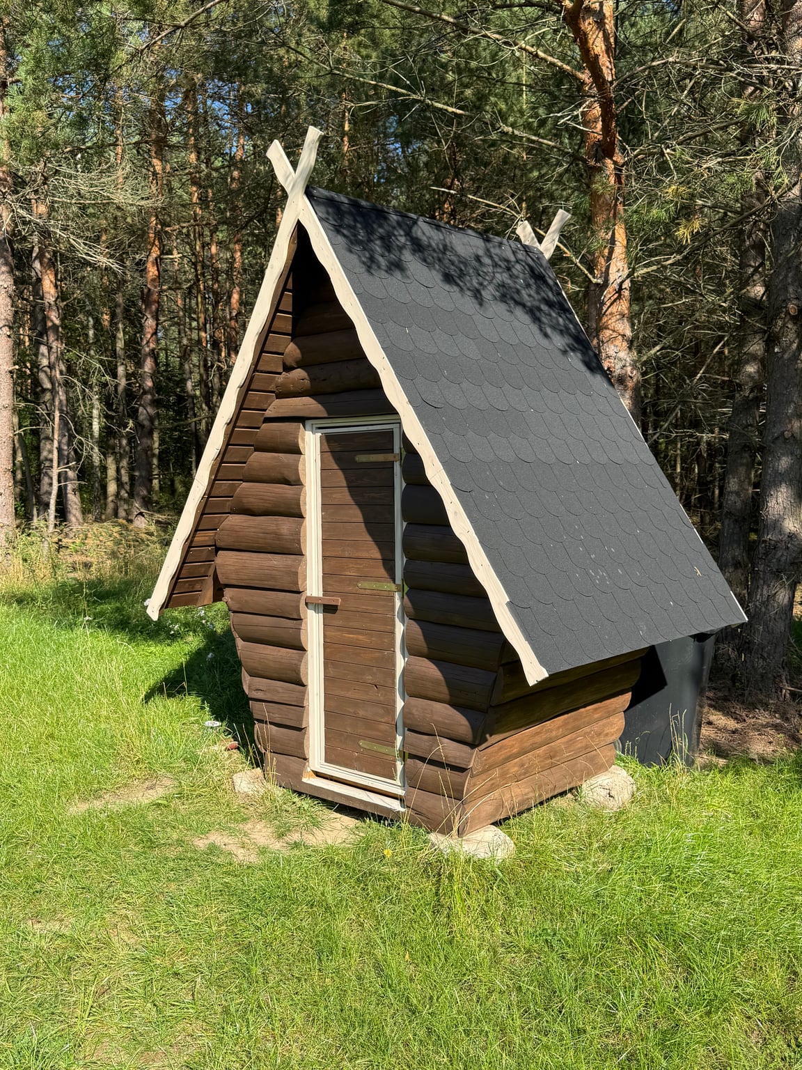 A wooden outdoor toilet with a tall roof built by Siarhei